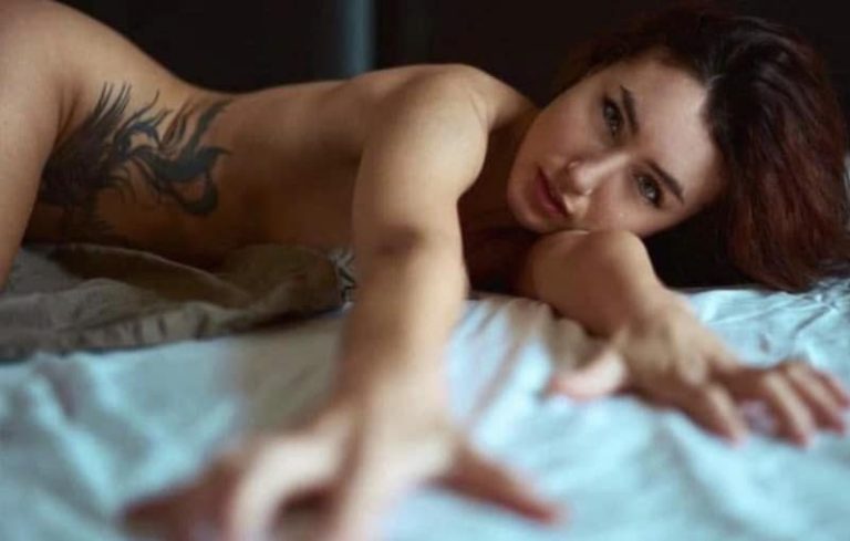 A woman with a tattoo poses on a bed, reaching towards the camera. boudoir in altoona pennsylvania, zxr photography, gary tritle